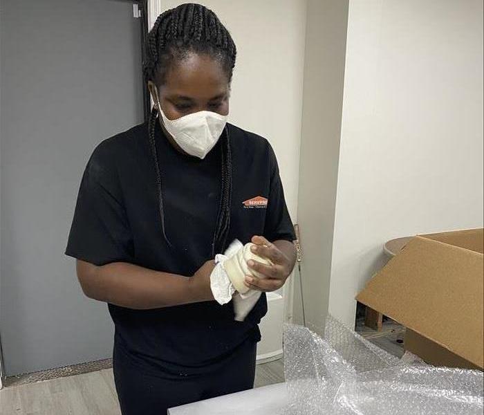 Woman in SERVPRO shirt wiping down household items and boxing them