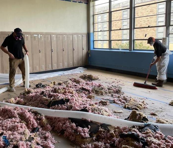 Two male SERVPRO employees cleaning up pink insulation