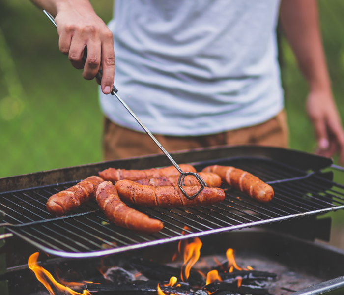 man using grill to cook hot dogs 